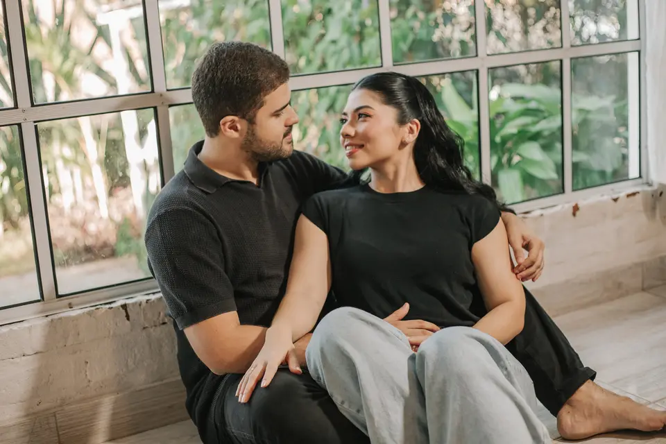 Jessica e Felipe sentados no chão, encostados um no outro, diante de uma janela com vista para o verde